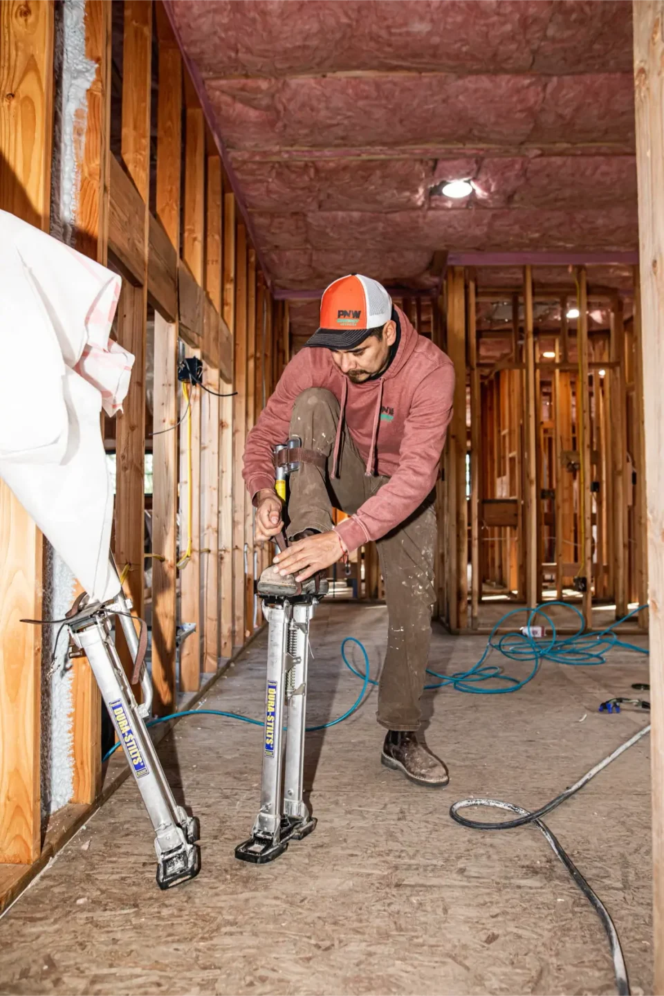 PNW Construction & Energy Services worker gettiong ready to install insulation in the beams while on stilts.